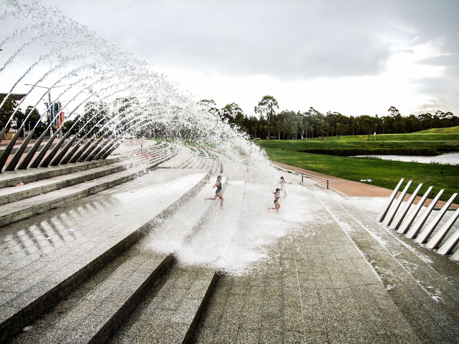 Des enfants s'amusant et courant sous les jets d'eau incurvés du site olympique des JO des Sydney en Australie par Jérémie Botte.