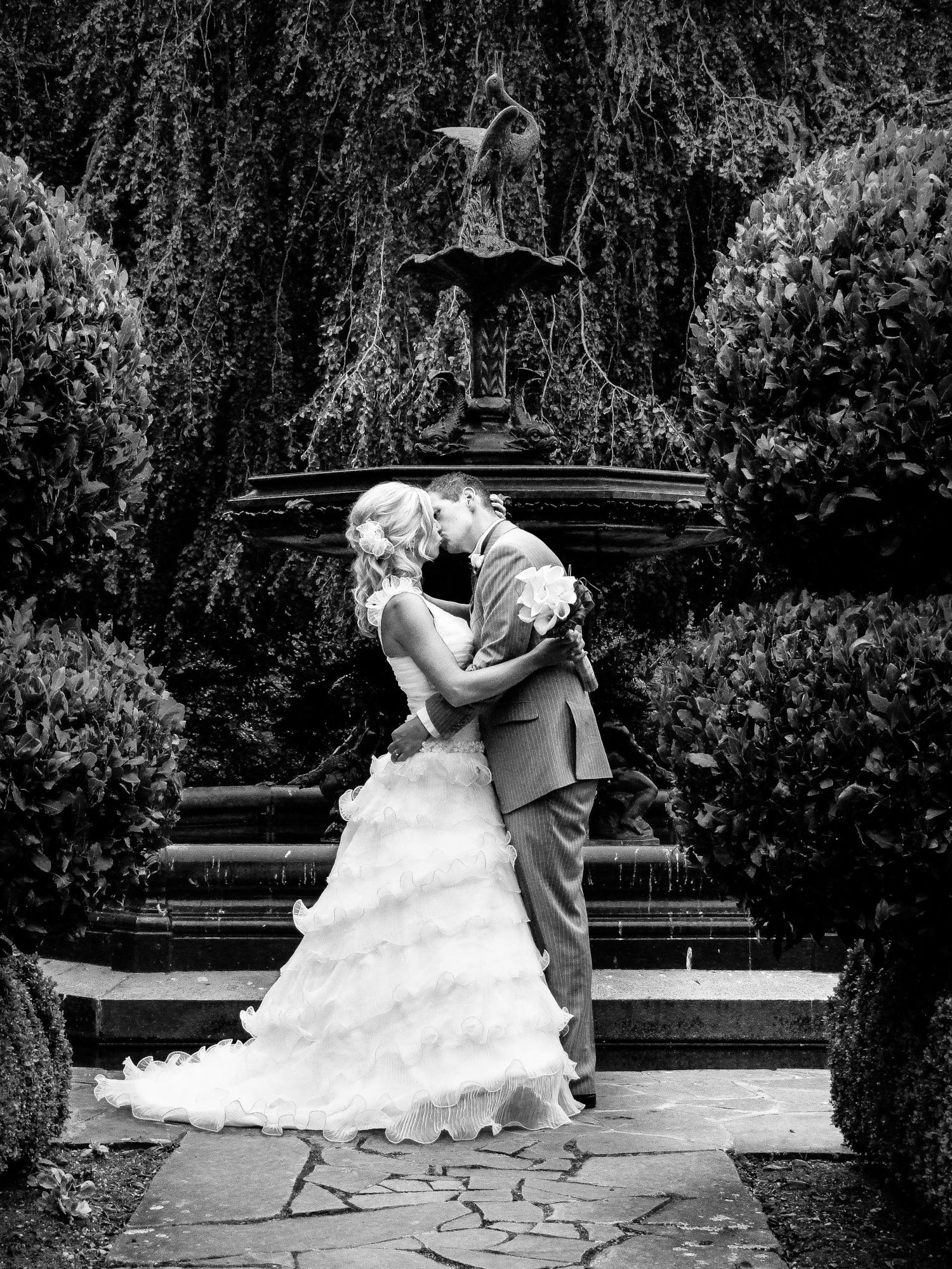 Portrait romantique en noir et blanc du couple s'embrassant devant une fontaine sculptée, par Jérémie Botte.