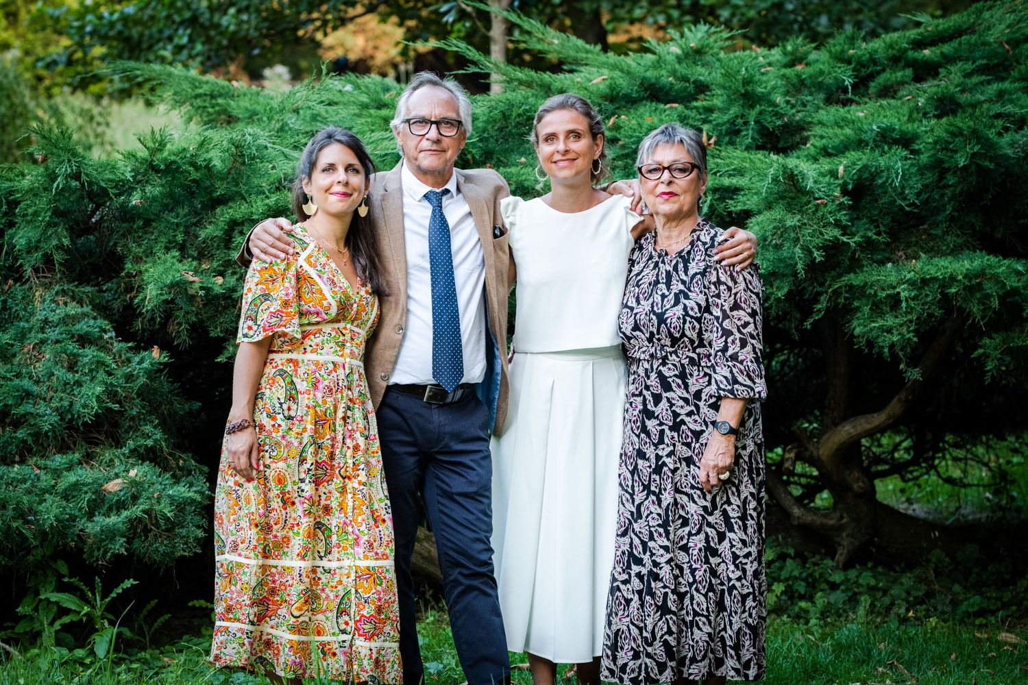 Photo de famille réunissant quatre personnes posant chaleureusement ensemble devant une haie verdoyante, par Jérémie Botte.