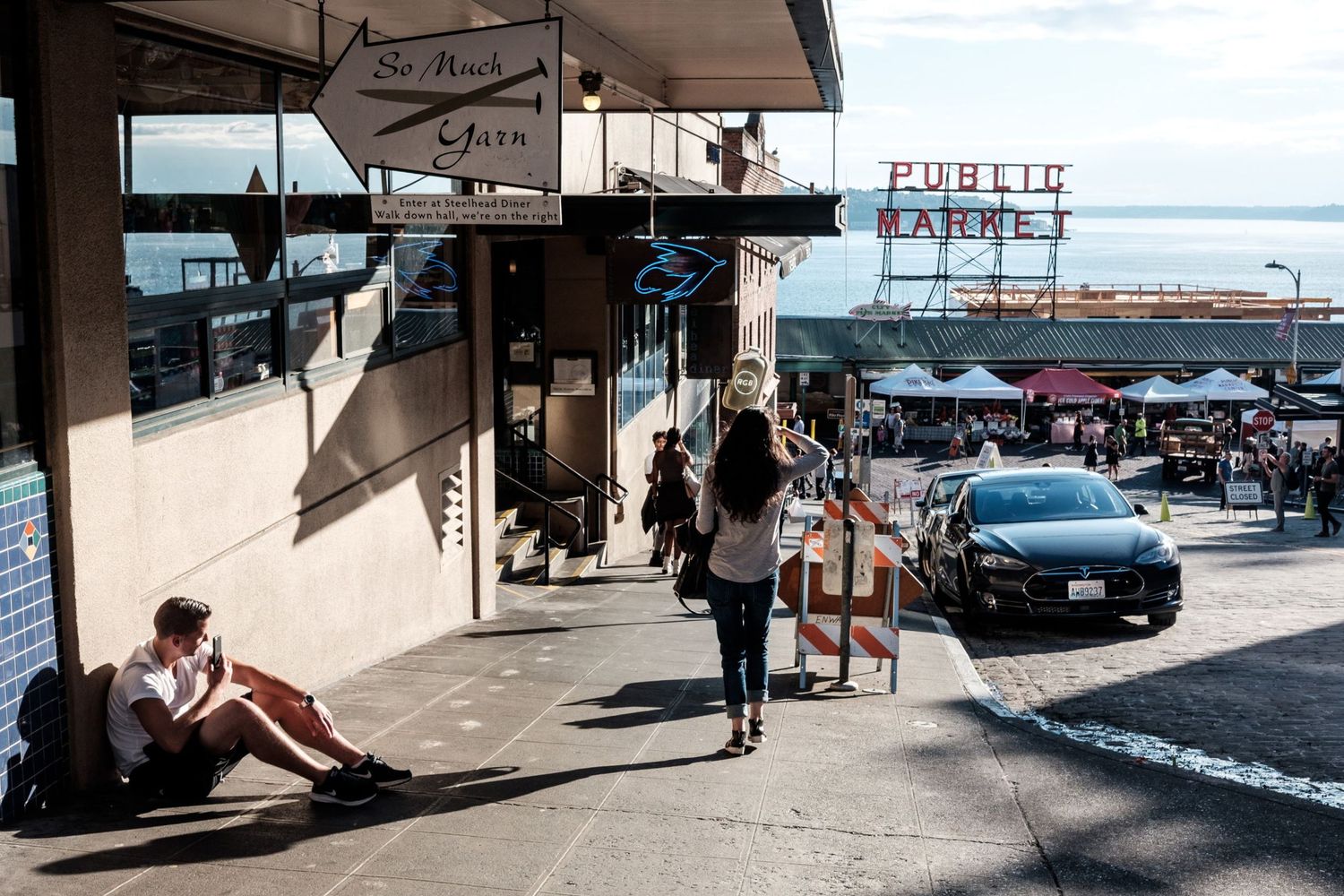 Une rue menant vers l'enseigne emblématique du Pike Place Public Market avec des passants et une voiture à Seattle, par Jérémie Botte.