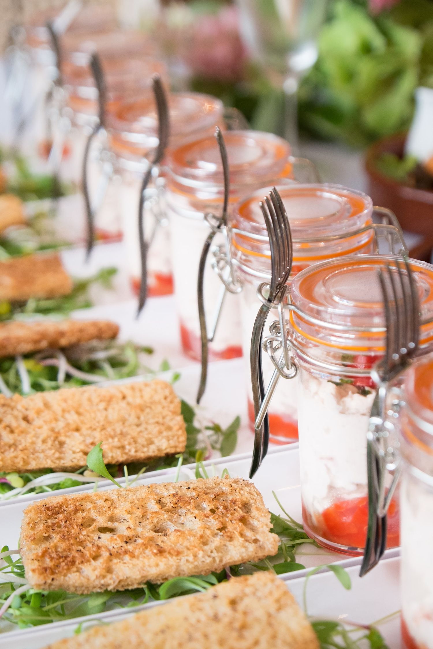 Une rangée de verrines à base de crème et de tomates, surmontées de petits toasts croustillants posés sur un lit de salade, photo de J Botte