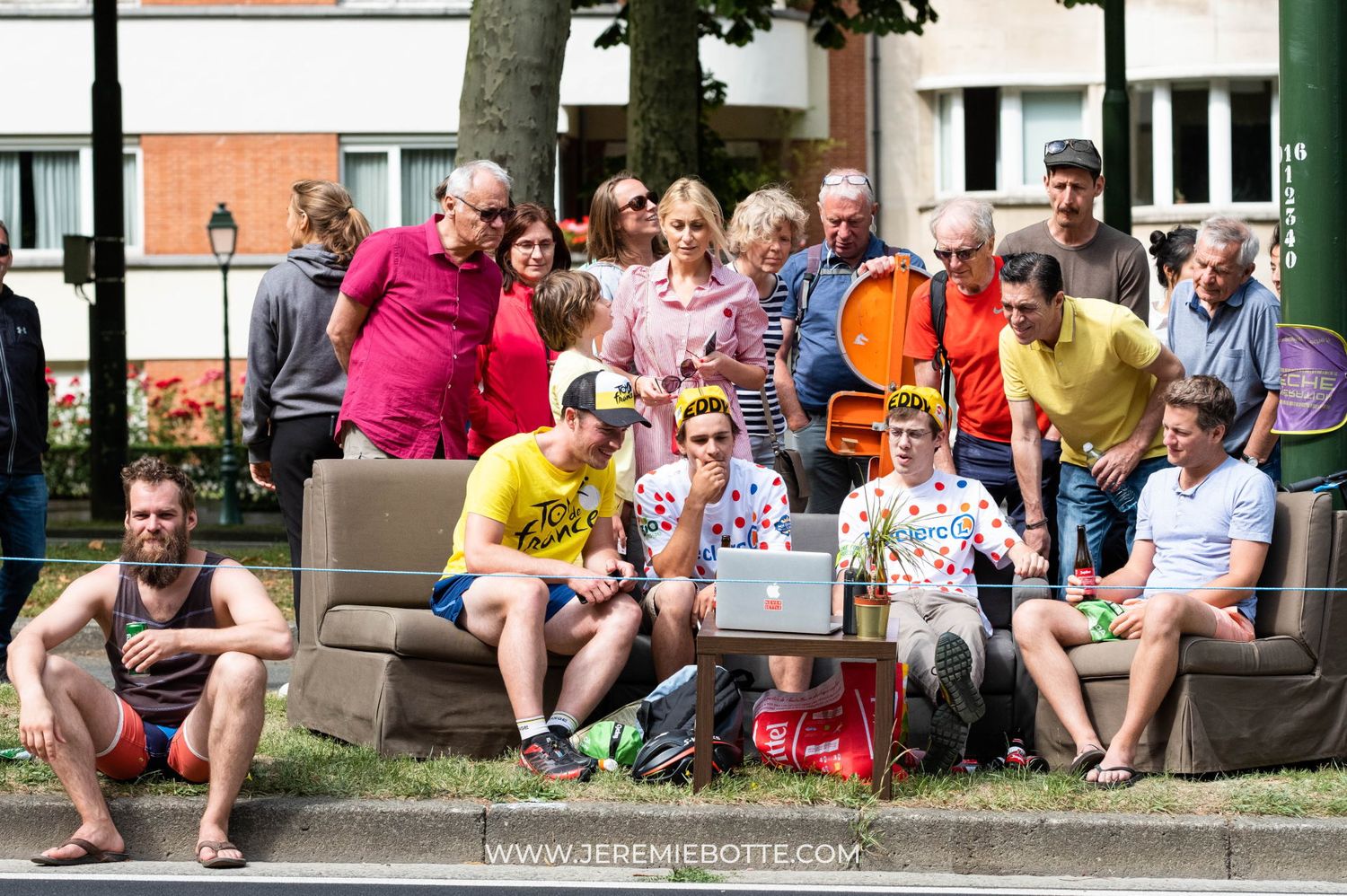 Un groupe de personnes installées sur des canapés en plein air regarde l'écran d'un ordinateur portable par Jérémie Botte.