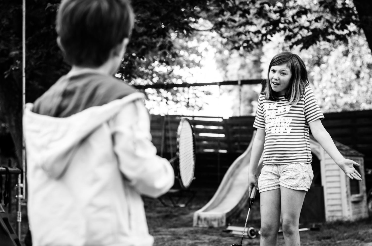 Deux enfants discutant dans un jardin avec une balançoire et un toboggan en arrière-plan, par Jérémie Botte.