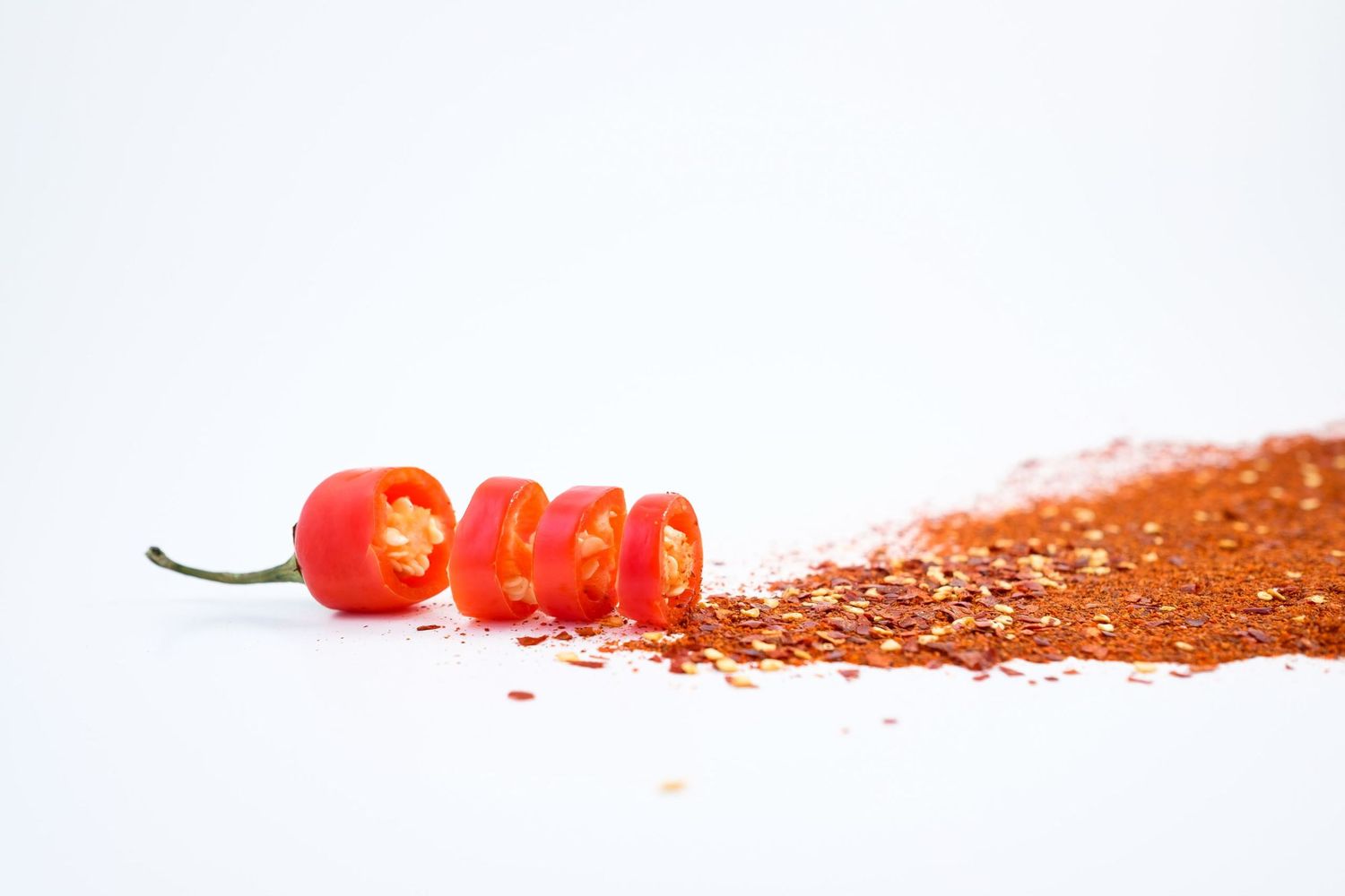 Présentation à plat montrant un piment rouge entier tranché en rondelles à côté de piment broyé, par Jérémie Botte.