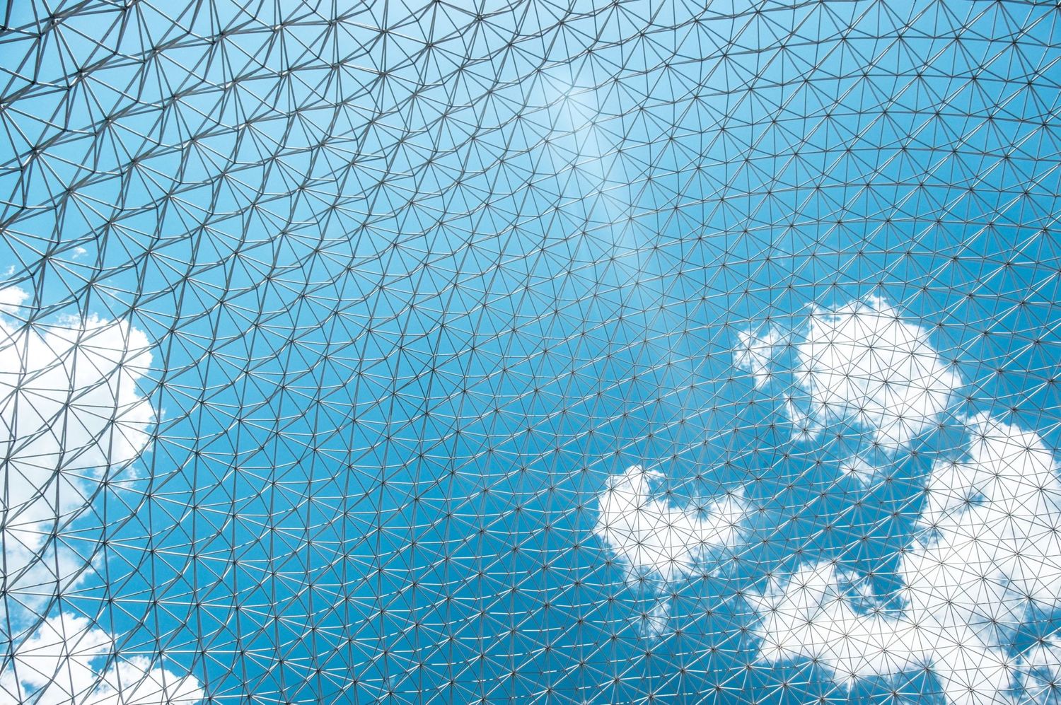 Une vue à travers la structure géodésique en réseau métallique de la Biosphère de Montréal sur fond de ciel bleu, par Jérémie Botte.