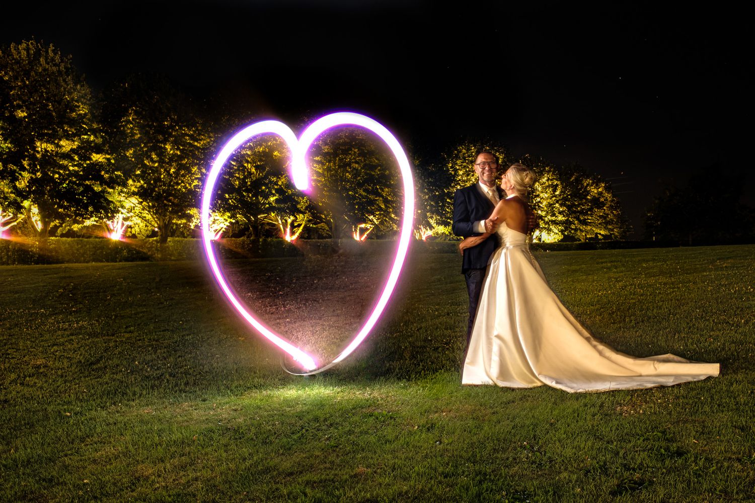 Photographie de mariage de mariés tout sourire de nuit en exterieur avec un coeur type light-painting par le photographe Jérémie Botte.