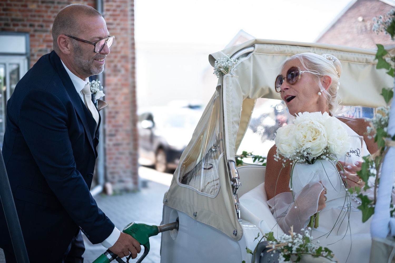 Photographie de mariage en exterieur de jour des deux mariés s'amusant à la pompe à essence par le photographe professionel Jérémie Botte.