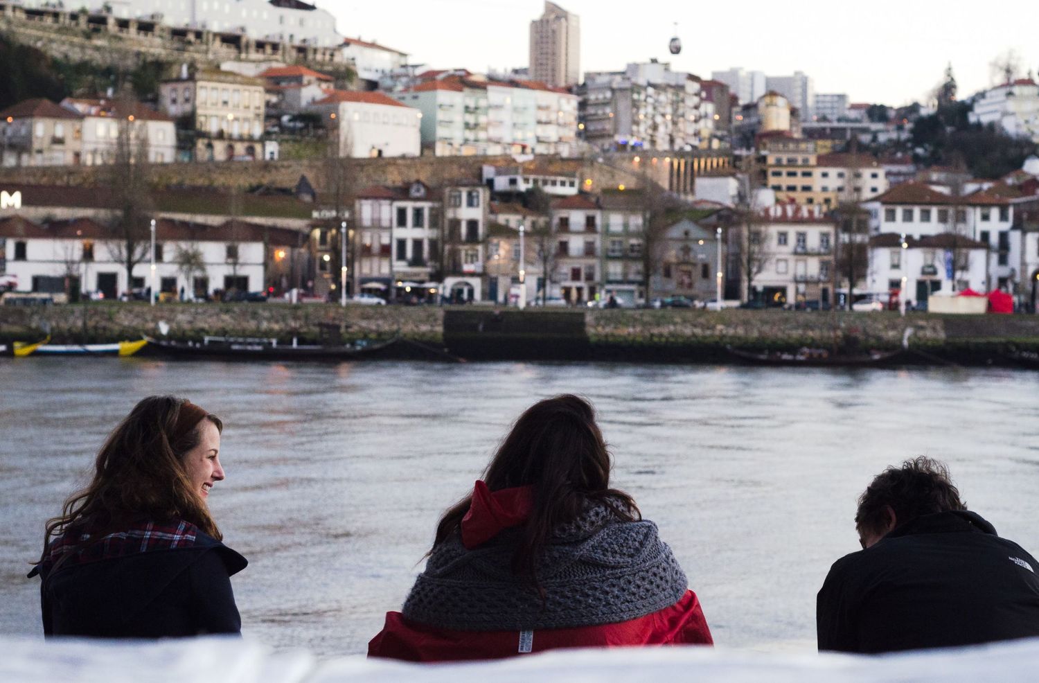 Trois personnes de dos contemplant le fleuve Douro et les collines habitées de Porto au Portugal, par Jérémie Botte.