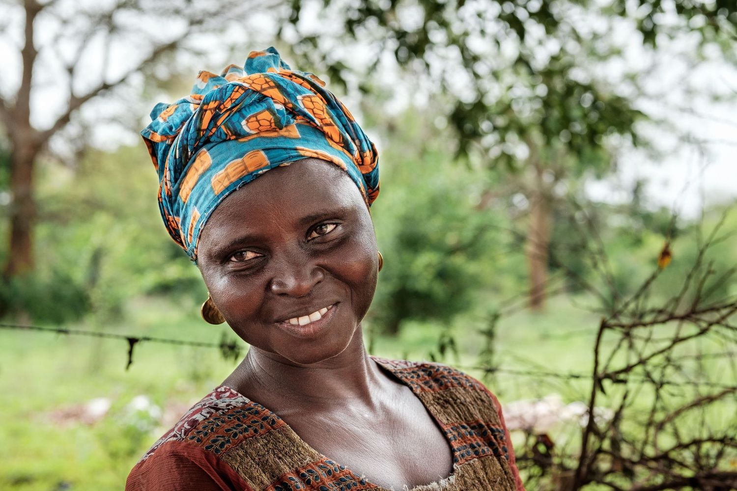 Portrait d'une femme souriante portant un turban coloré dans un cadre de verdure, par Jérémie Botte.