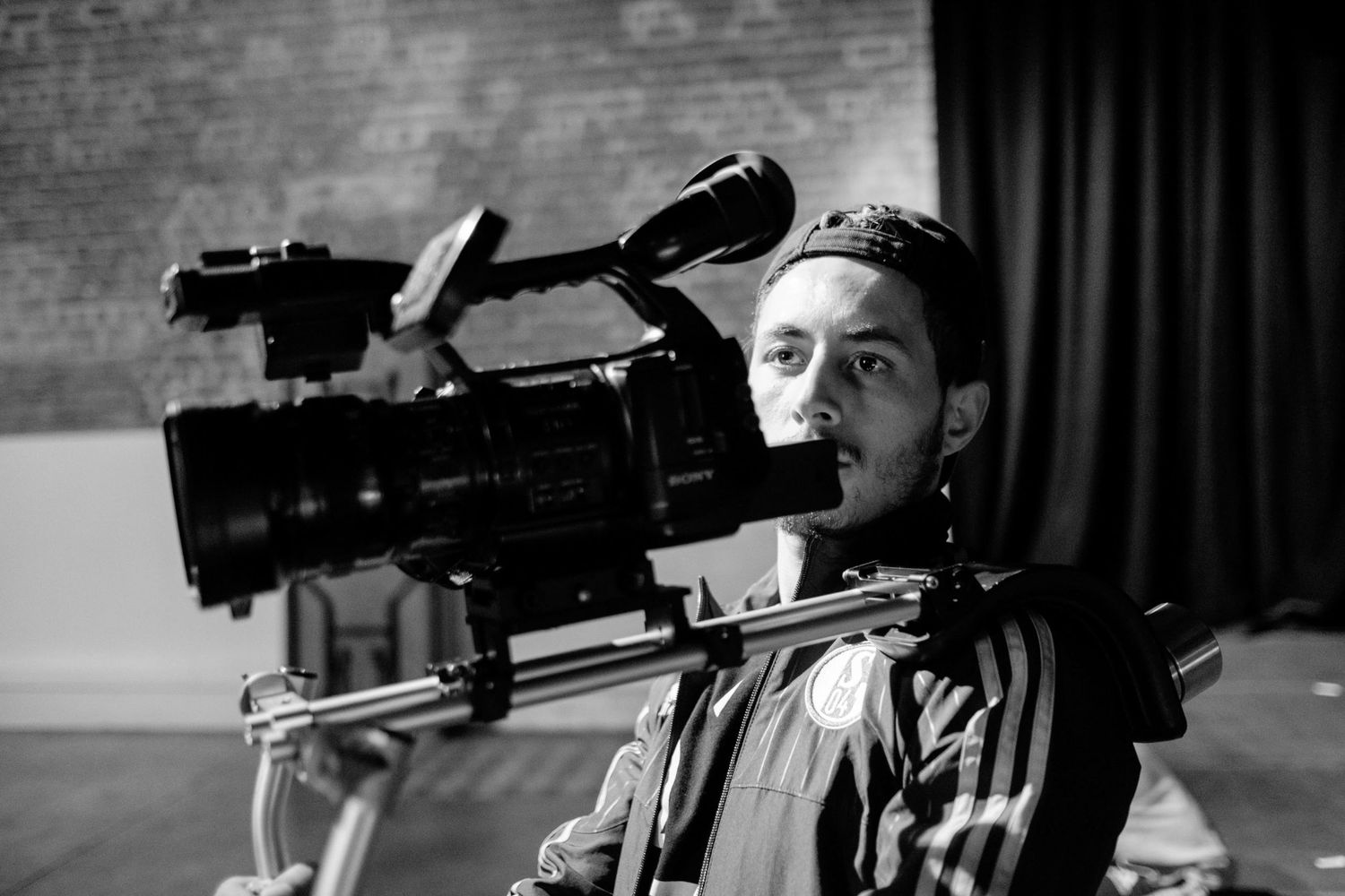 Homme de profil cadrant avec une caméra vidéo professionnelle, photo noir et blanc, par Jérémie Botte.