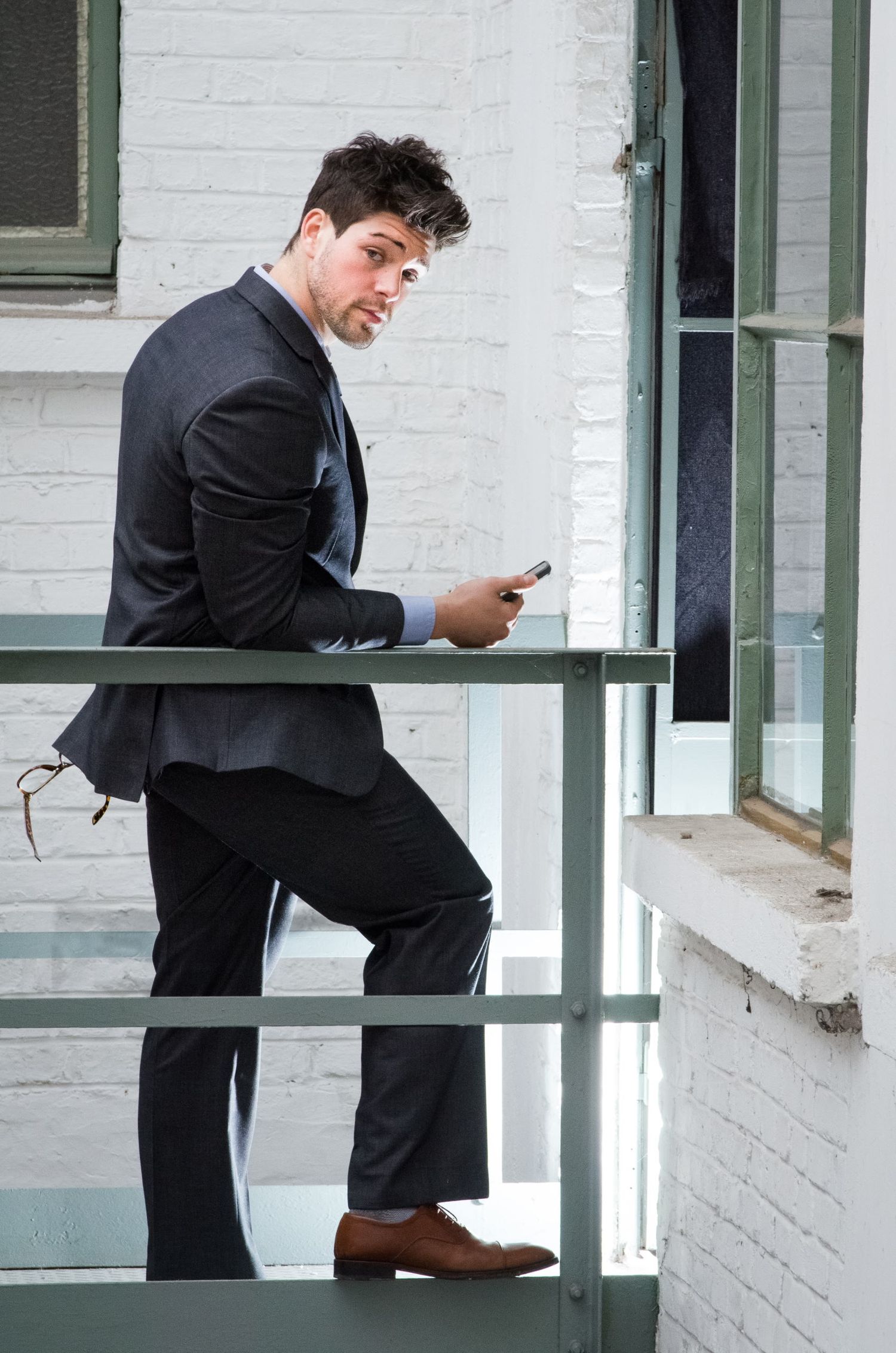 Un homme en costume noir regarde en arrière sur une passerelle extérieure tout en tenant son téléphone par Jérémie Botte