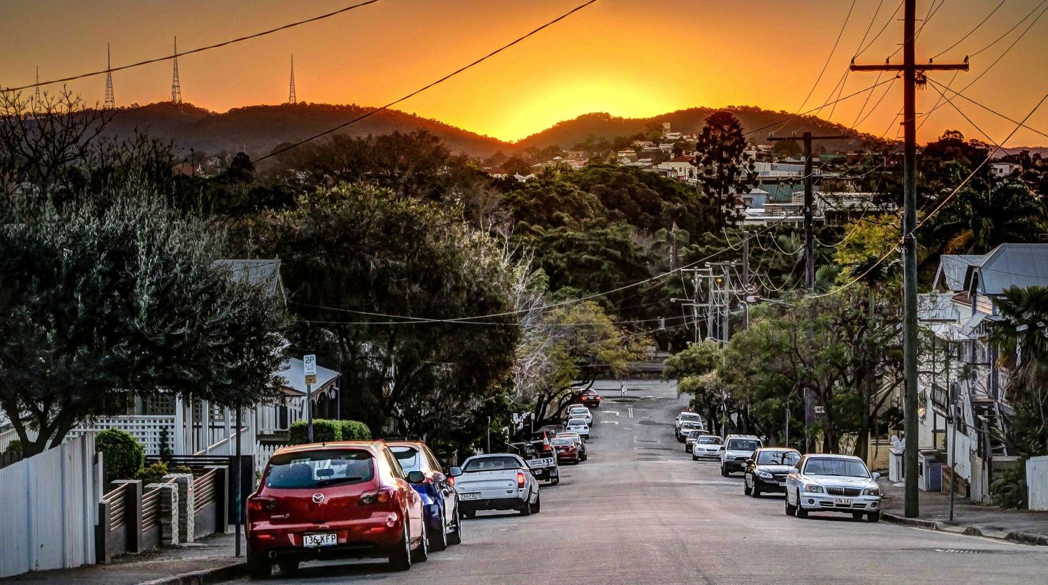 Rue résidentielle en pente bordée de voitures sous un coucher de soleil flamboyant à Brisbane en Australie par Jérémie Botte.