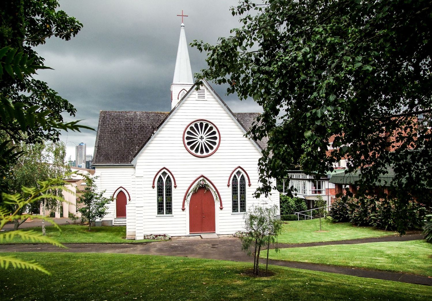 Une église blanche aux portes et finitions rouges entourée de verdure sous un ciel chargé en Nouvelle-Zélande, par Jérémie Botte
