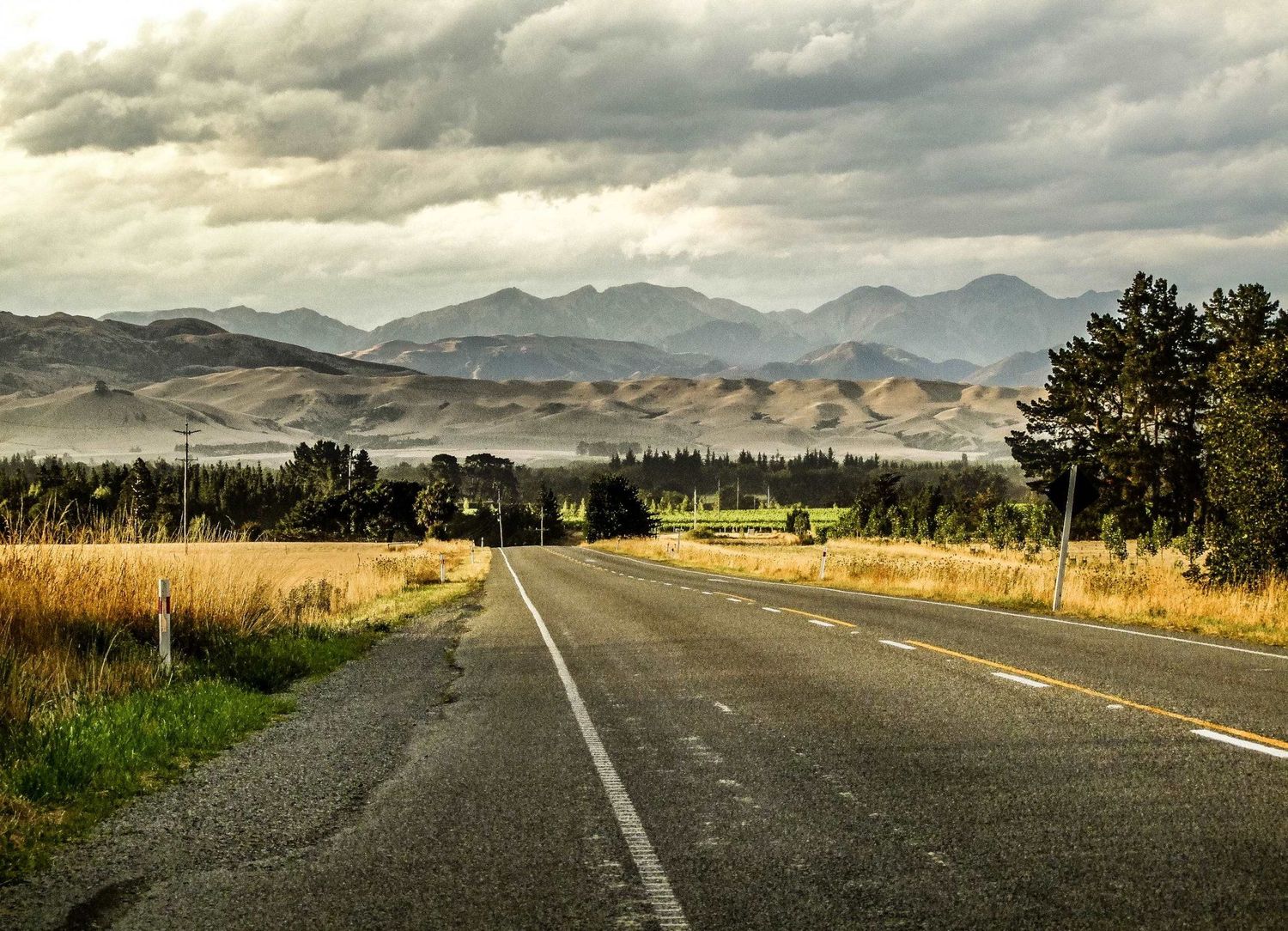 Photo de voyage en Nouvelle-Zélande montrant une longue route asphaltée déserte face à une chaîne de montagnes par Jérémie Botte.