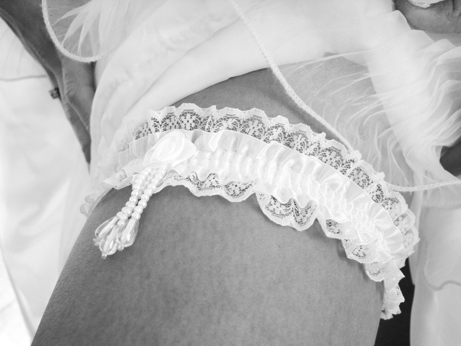 Gros plan sur une jarretière de mariage blanche ornée de perles sur la cuisse d'une femme, par Jérémie Botte.