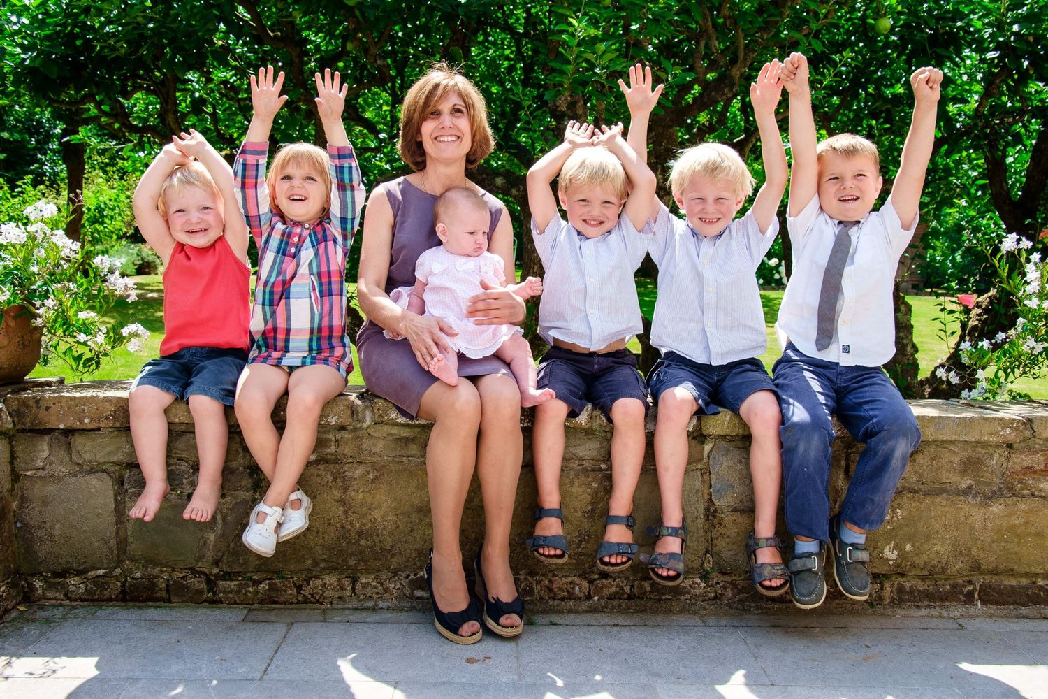 Photo de famille en extérieur avec une femme et des enfants joyeux assis sur un muret par le photographe Jérémie Botte.
