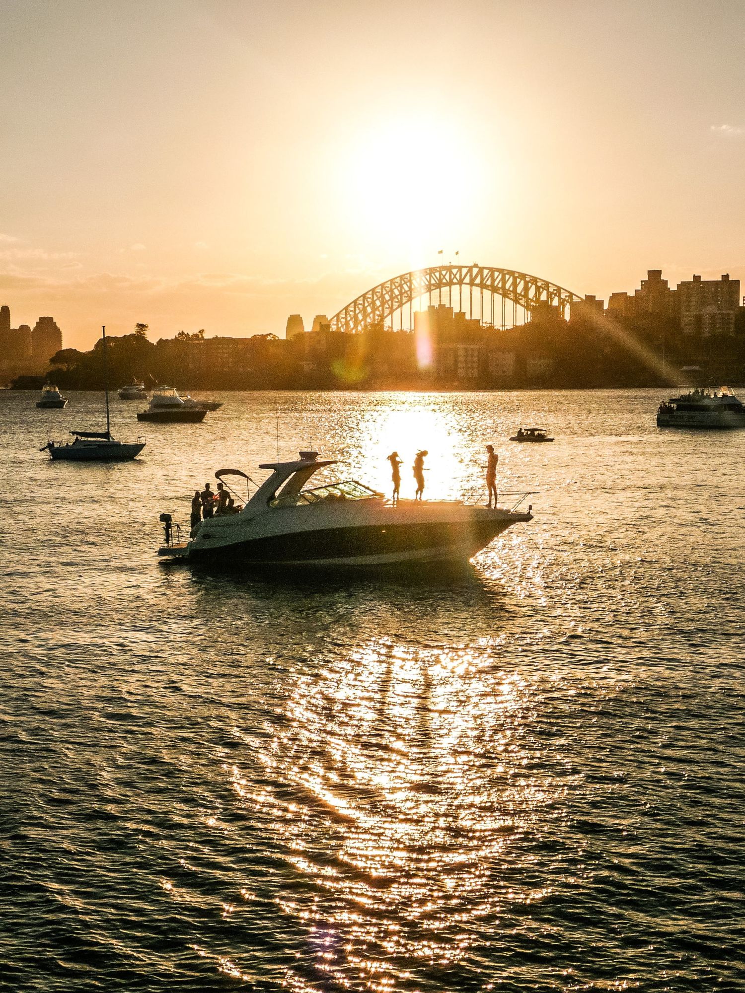 Une vue à contre-jour d'un bateau sur la baie de Sydney au coucher du soleil, avec le Harbour Bridge en fond d'image, par Jérémie Botte