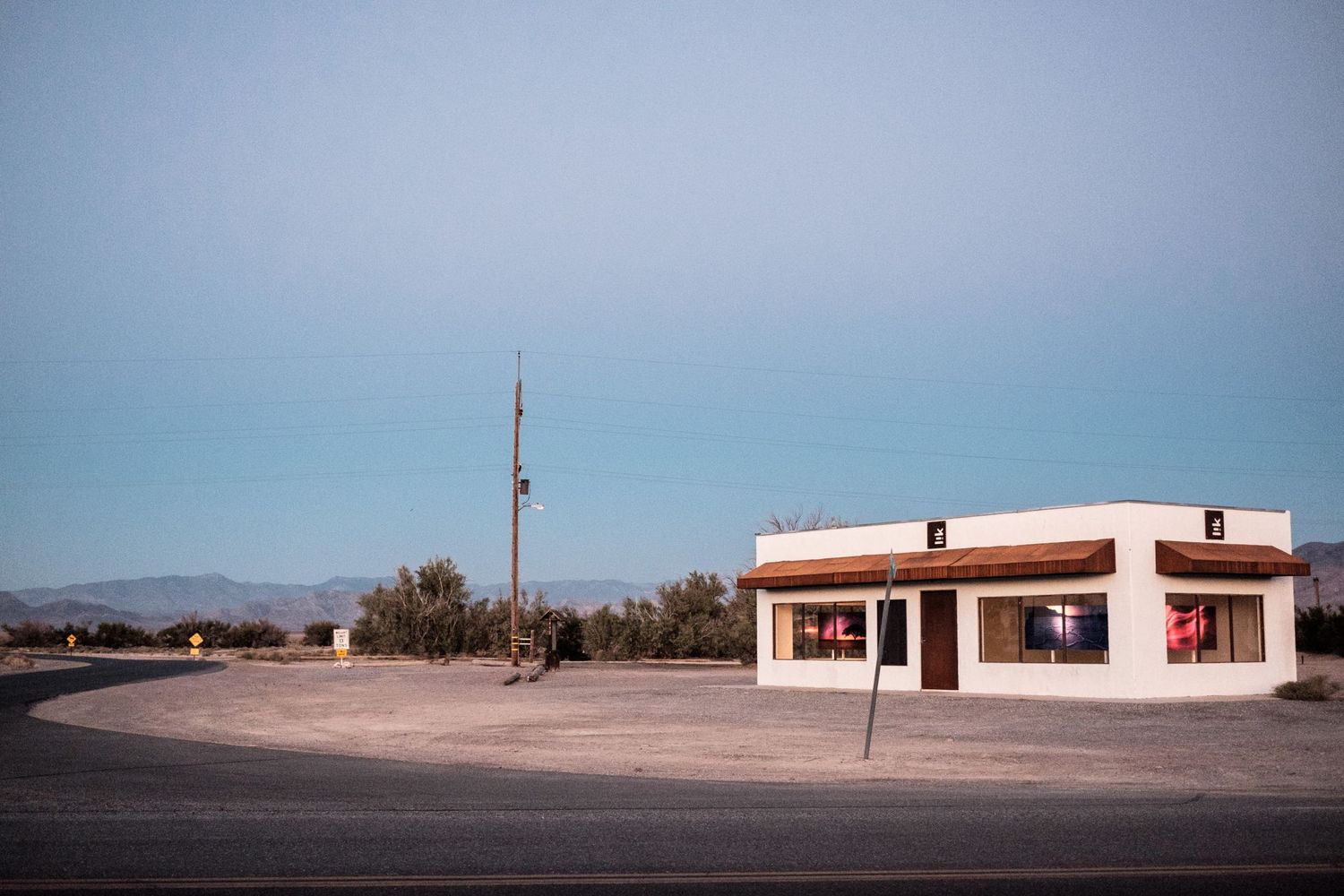 Un bâtiment blanc isolé au bord d'une route déserte à l'approche du crépuscule aux États-Unis, par Jérémie Botte.