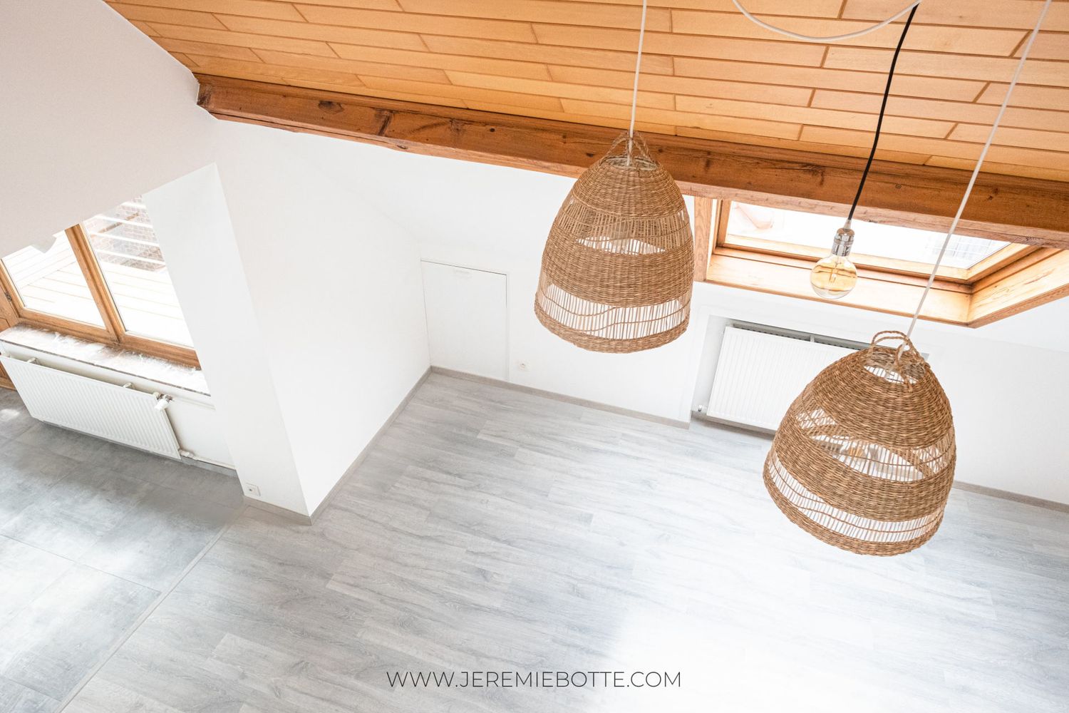 Vue plongeante sur l'espace de vie mansardé d'un duplex avec plancher gris et suspensions en osier, par Jérémie Botte.