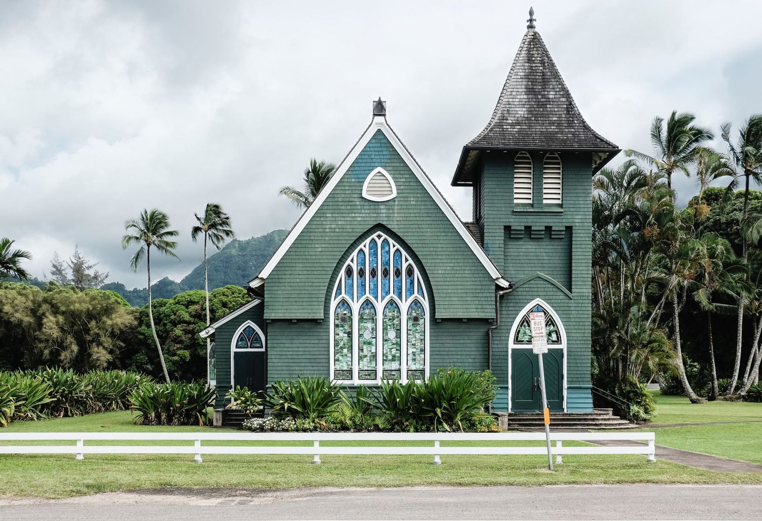 Une église en bois d'un vert profond de style gothique entourée de palmiers sous un ciel nuageux à Hawaï, par Jérémie Botte.