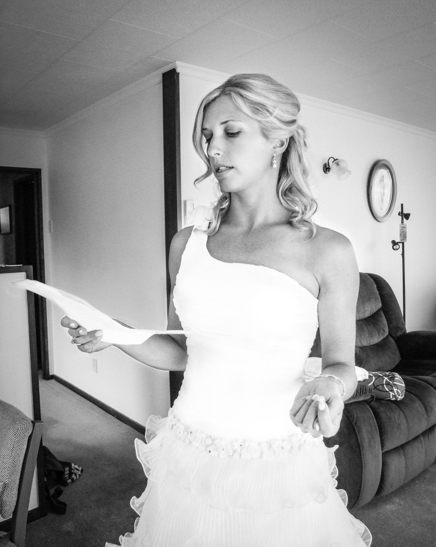 Une mariée dans sa robe asymétrique lisant attentivement une lettre en intérieur, photo noir et blanc par Jérémie Botte.