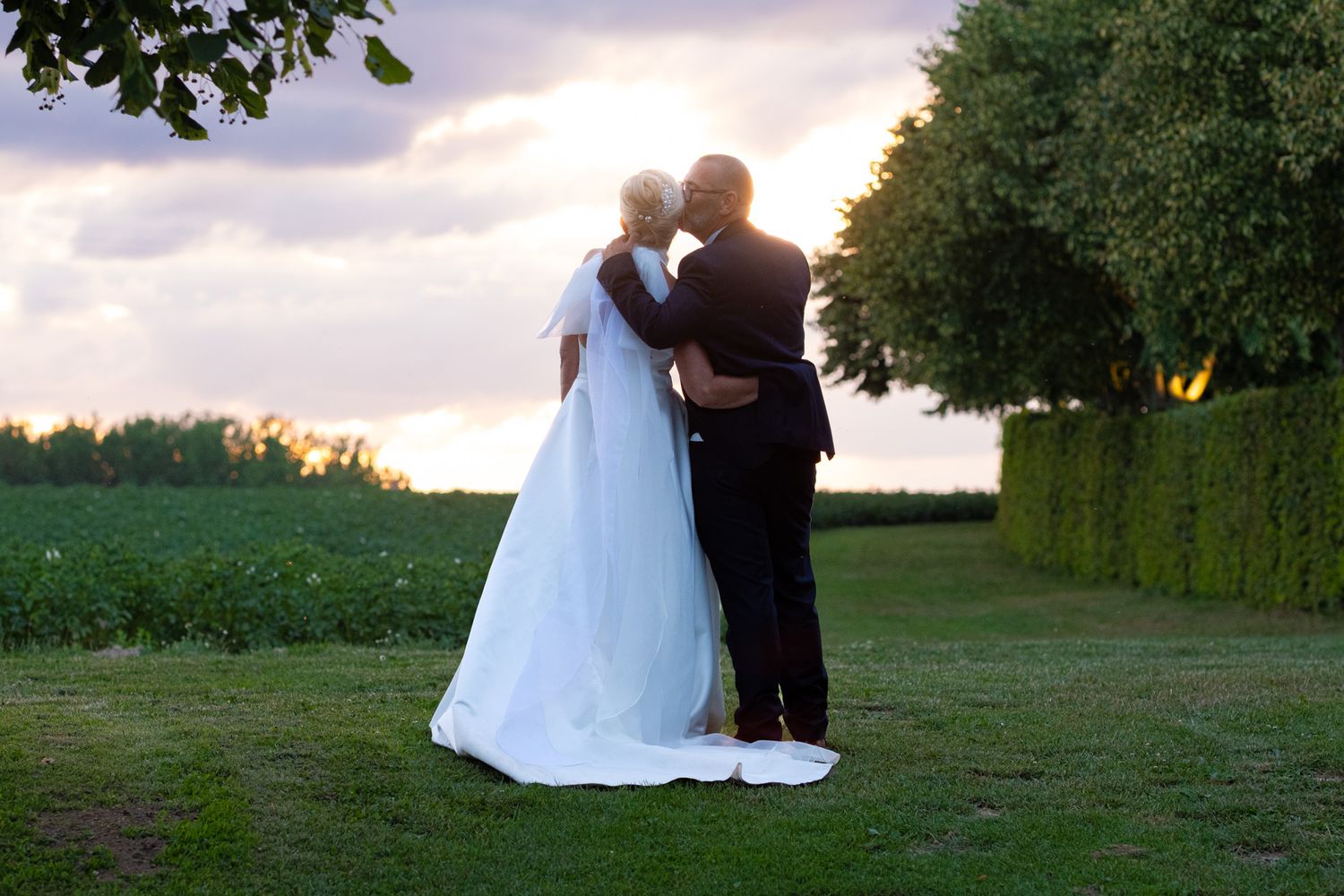 Photographie de mariage en exterieur durant la Goldent Hour de deux mariés s'embrassant de dos par le photographe professionel Jérémie Botte