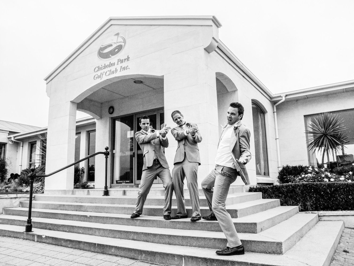 Trois hommes en costume s'amusant sur les marches du Chisholm Park Golf Club, photo de mariage en noir et blanc par Jérémie Botte.