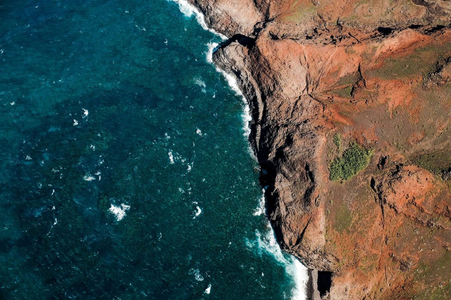 Photographie aérienne à Kauai aux États-Unis montrant des falaises de roche rouge bordées par une mer bleu foncé par Jérémie Botte.