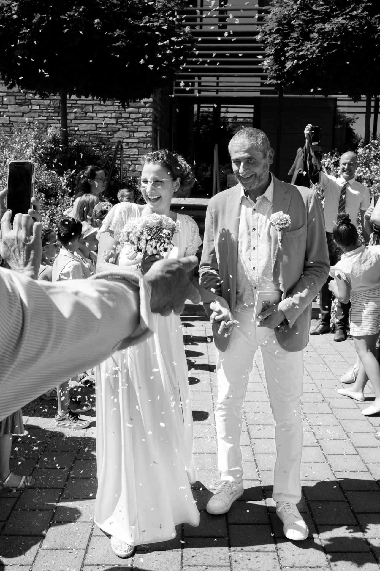Photographie en noir et blanc d'un couple de mariés souriant sous une pluie de confettis, par Jérémie Botte.