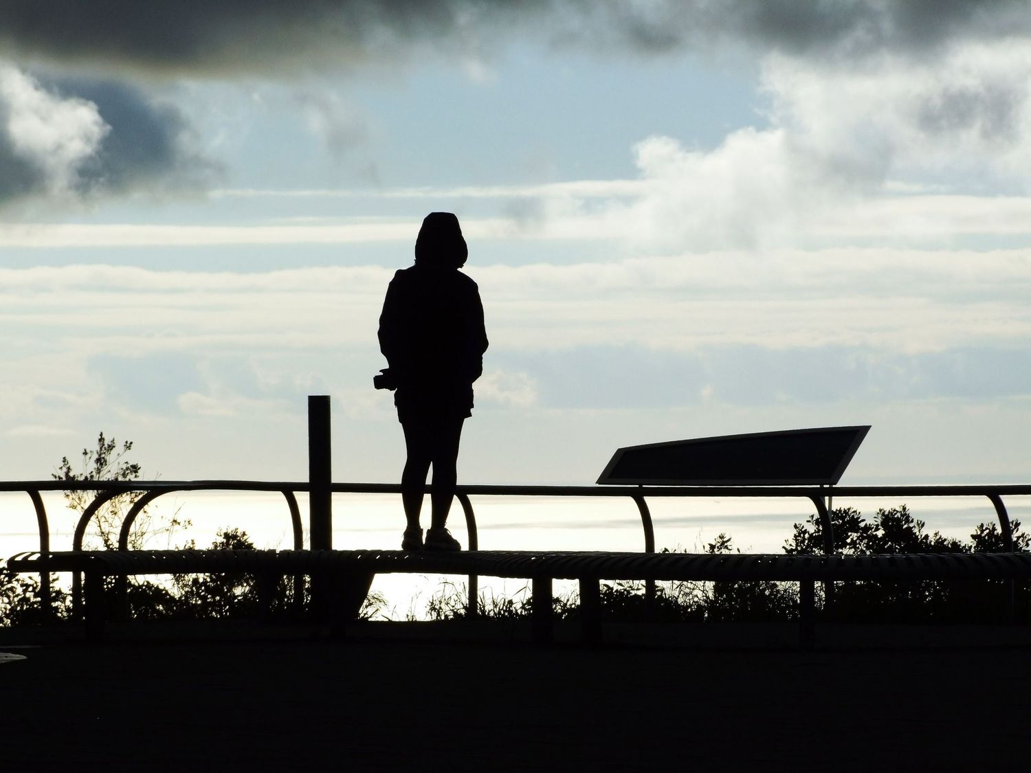 Silhouette d'une personne debout sur un banc face à l'océan sous un ciel nuageux par Jérémie Botte.
