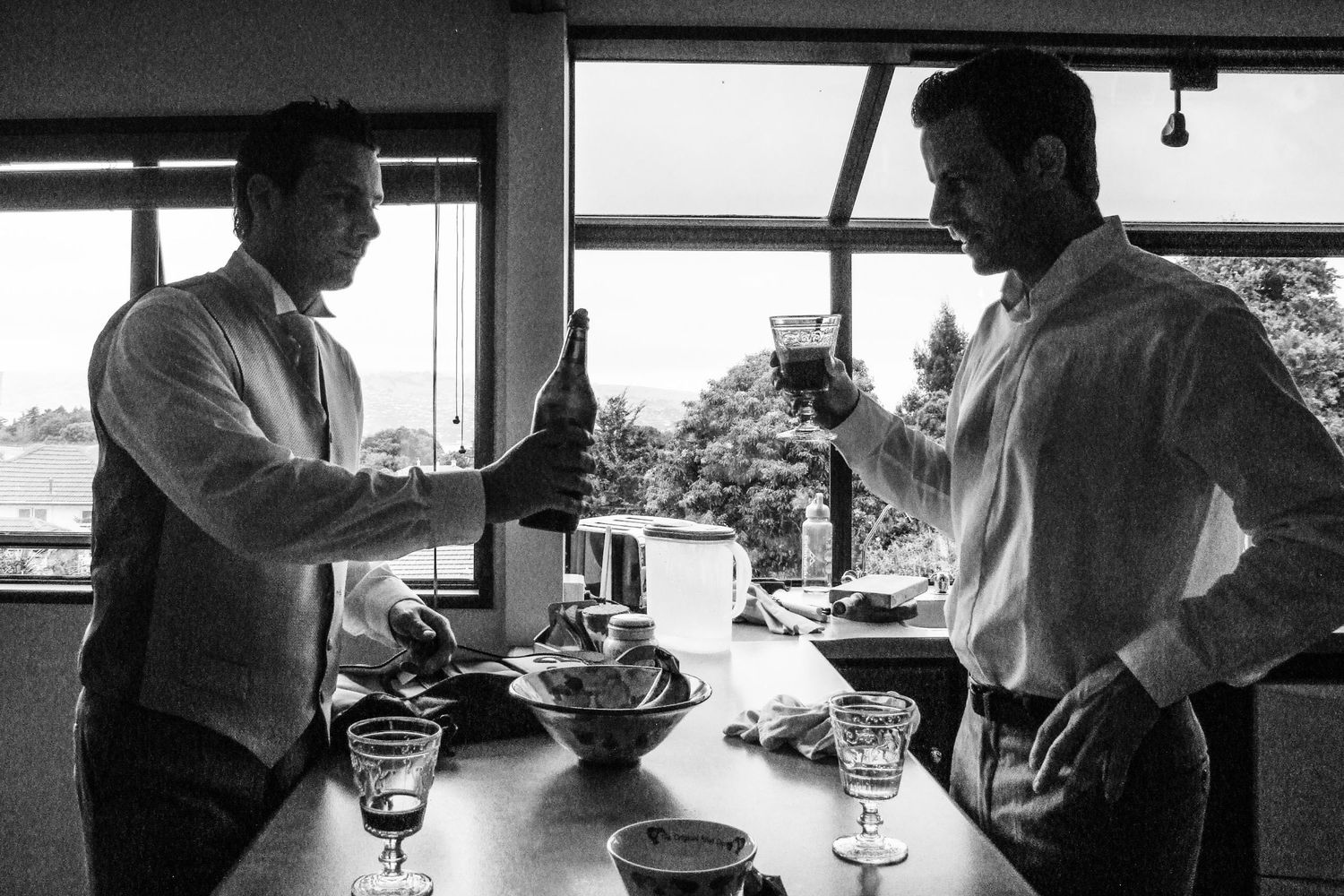 Deux hommes en costume trinquant avec des verres en intérieur, éclairés à contre-jour par une fenêtre, par Jérémie Botte.