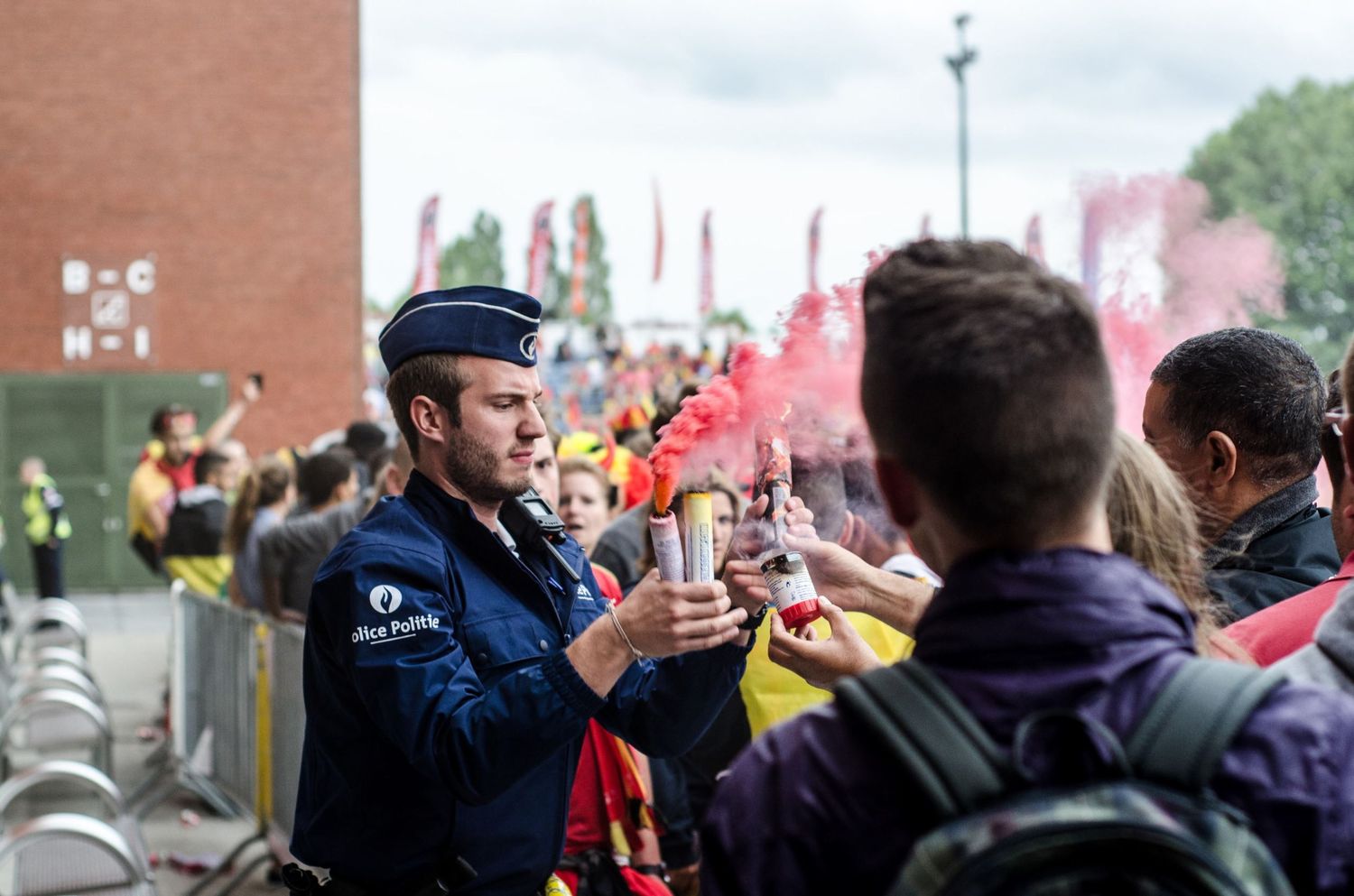 Un policier belge retire un fumigène rouge des mains de supporters lors d'un match de foot par Jérémie Botte.