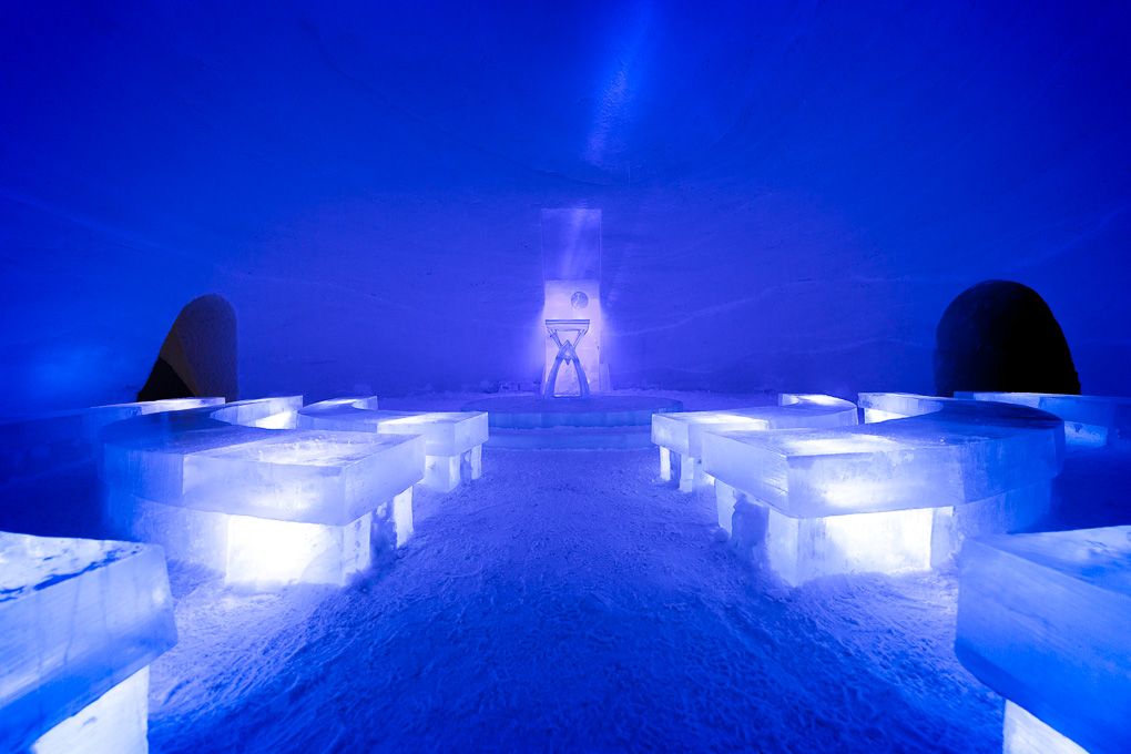 A series of glowing blue ice hotel structures illuminated at night creates a magical winter atmosphere. Ice Village excursion photography.
