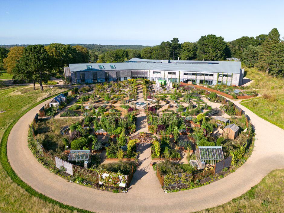 Aerial view of a circular garden with curved pathways and multiple planting beds next to a modern white building.