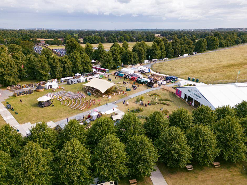 Aerial panoramic view shows an outdoor concert venue with amphitheater seating surrounded by lush green forest.