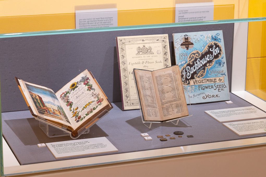RHS Wisley museum display case with antique books and manuscripts arranged in a curated exhibition setting.