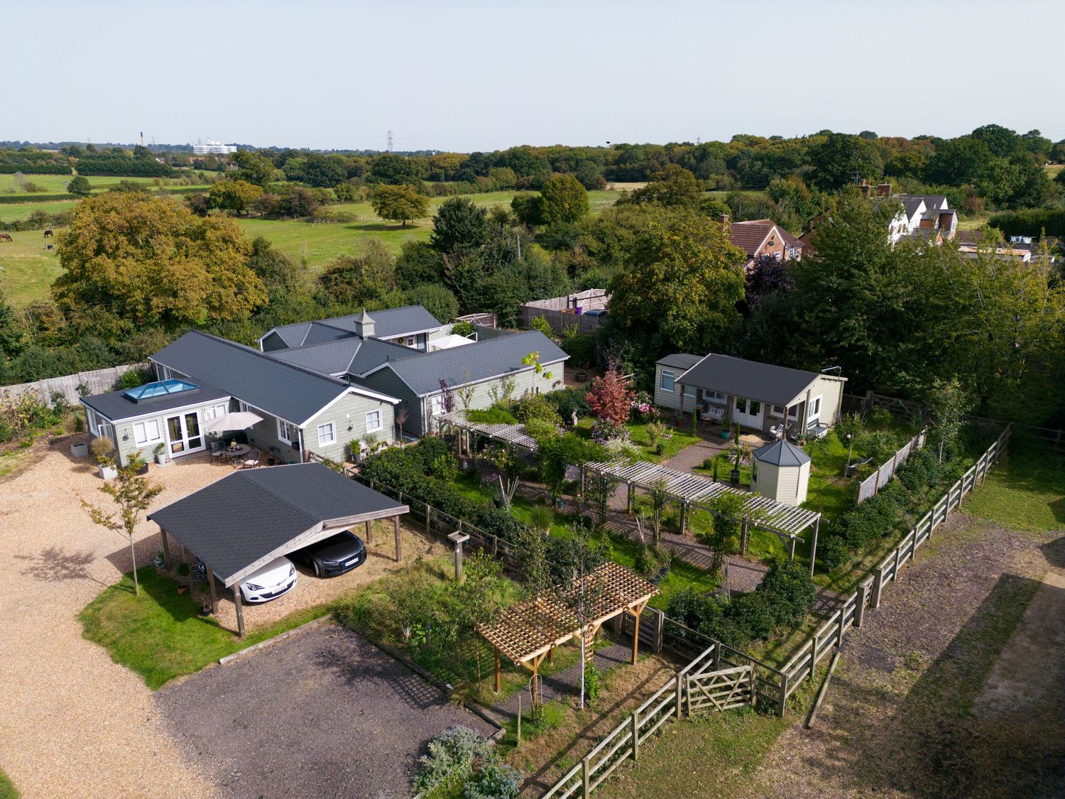Aerial view of rural residential property with landscaped gardens, outbuildings and surrounding countryside.