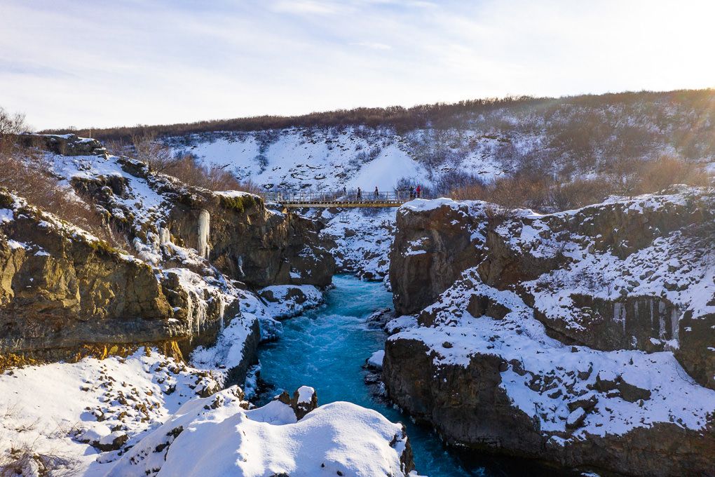 Panoramic winter landscape of the Hraunfossar Waterfalls with a turquoise river winding through rugged cliffs and mountains.
