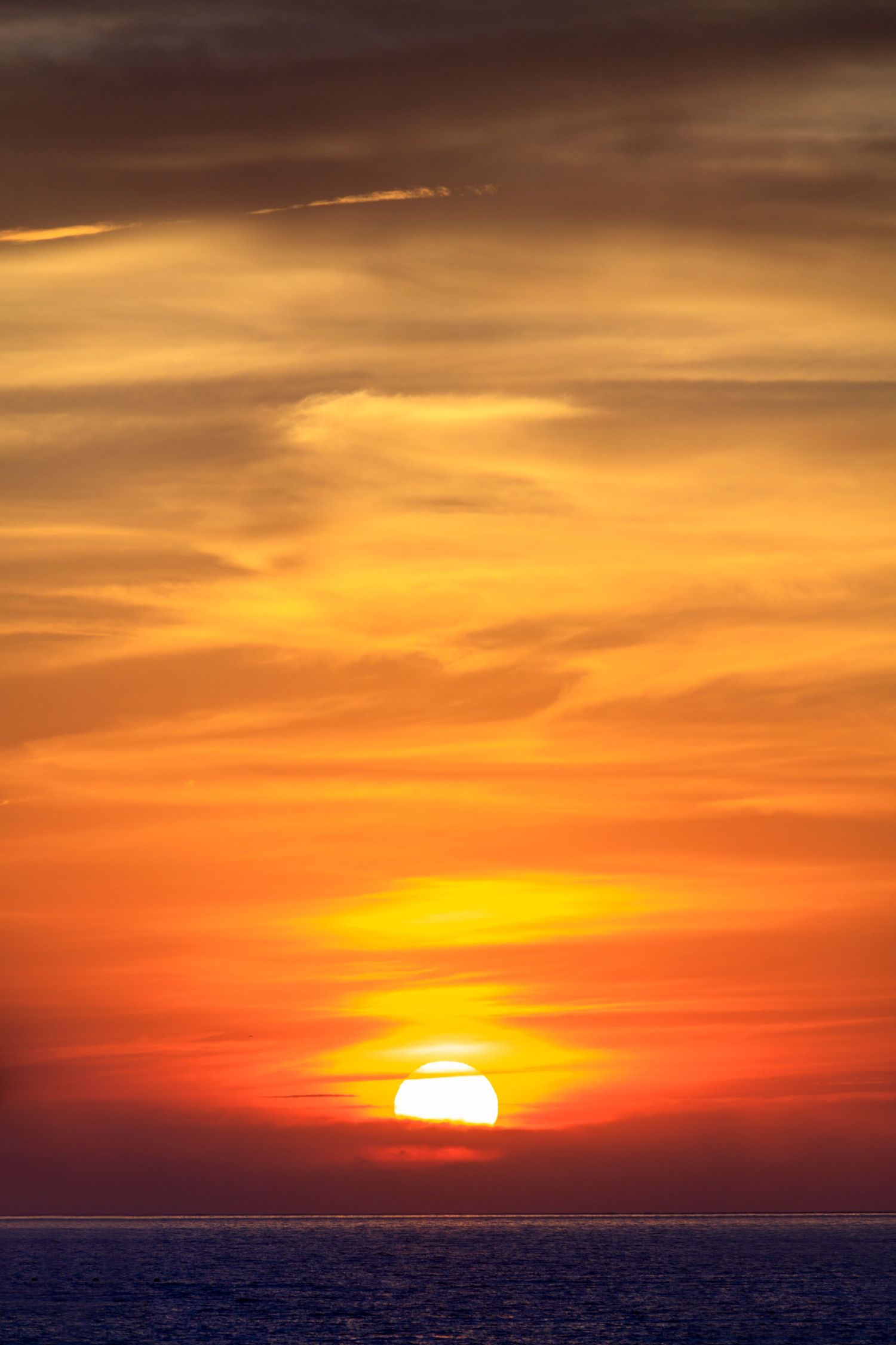 Stunning ocean sunset with vibrant orange and red sky, sun touching the horizon over calm sea waters.
