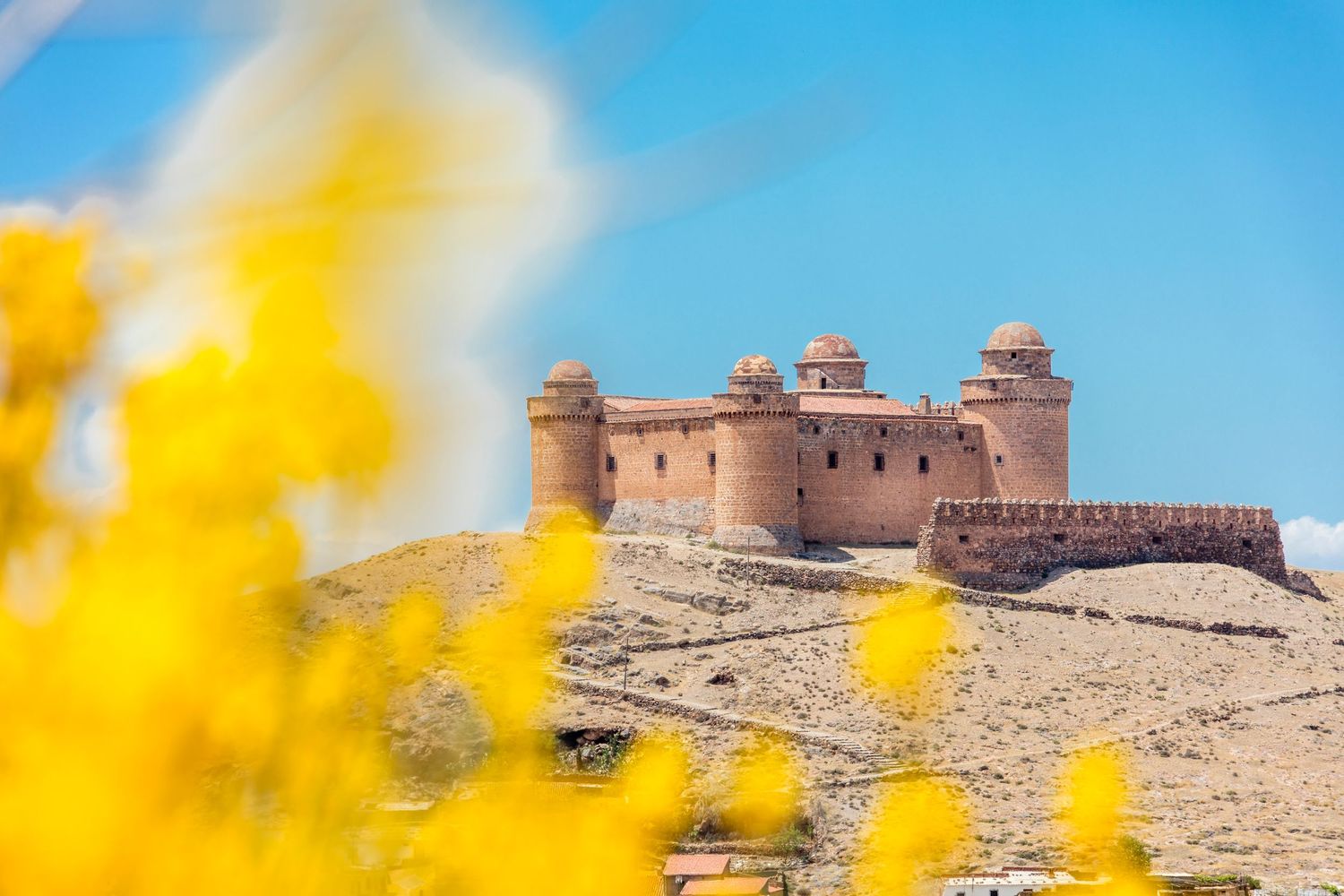 La Calahorra Renaissance castle on a hilltop framed by yellow flowers in Spain.