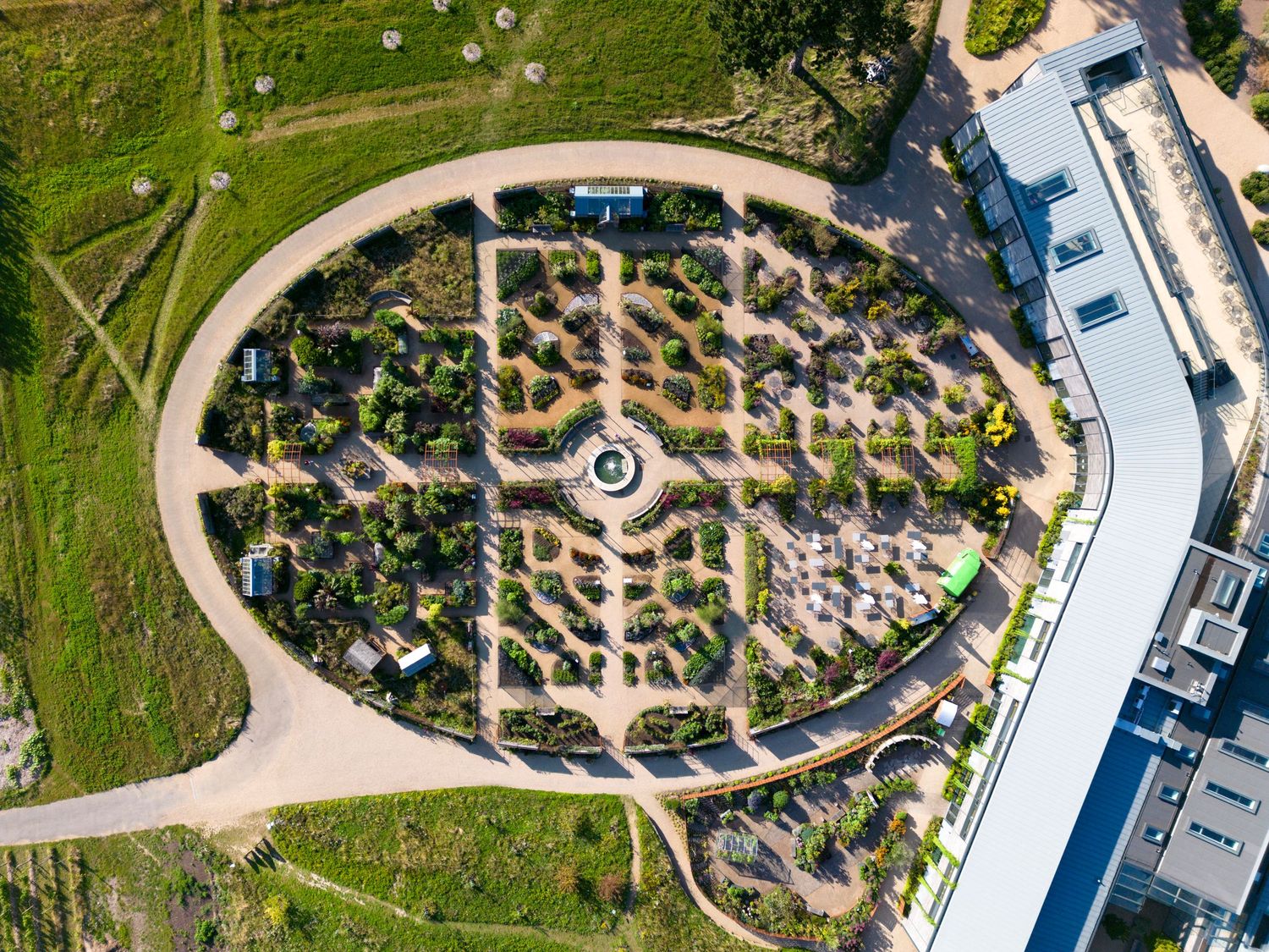 Aerial drone photograph of a formal garden featuring geometric pathways, ornamental planting and a central fountain beside a glasshouse.