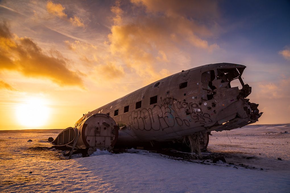 Dramatic sunset silhouettes the rusted wreckage of an abandoned DC-3 airplane on a black sand beach in Iceland.