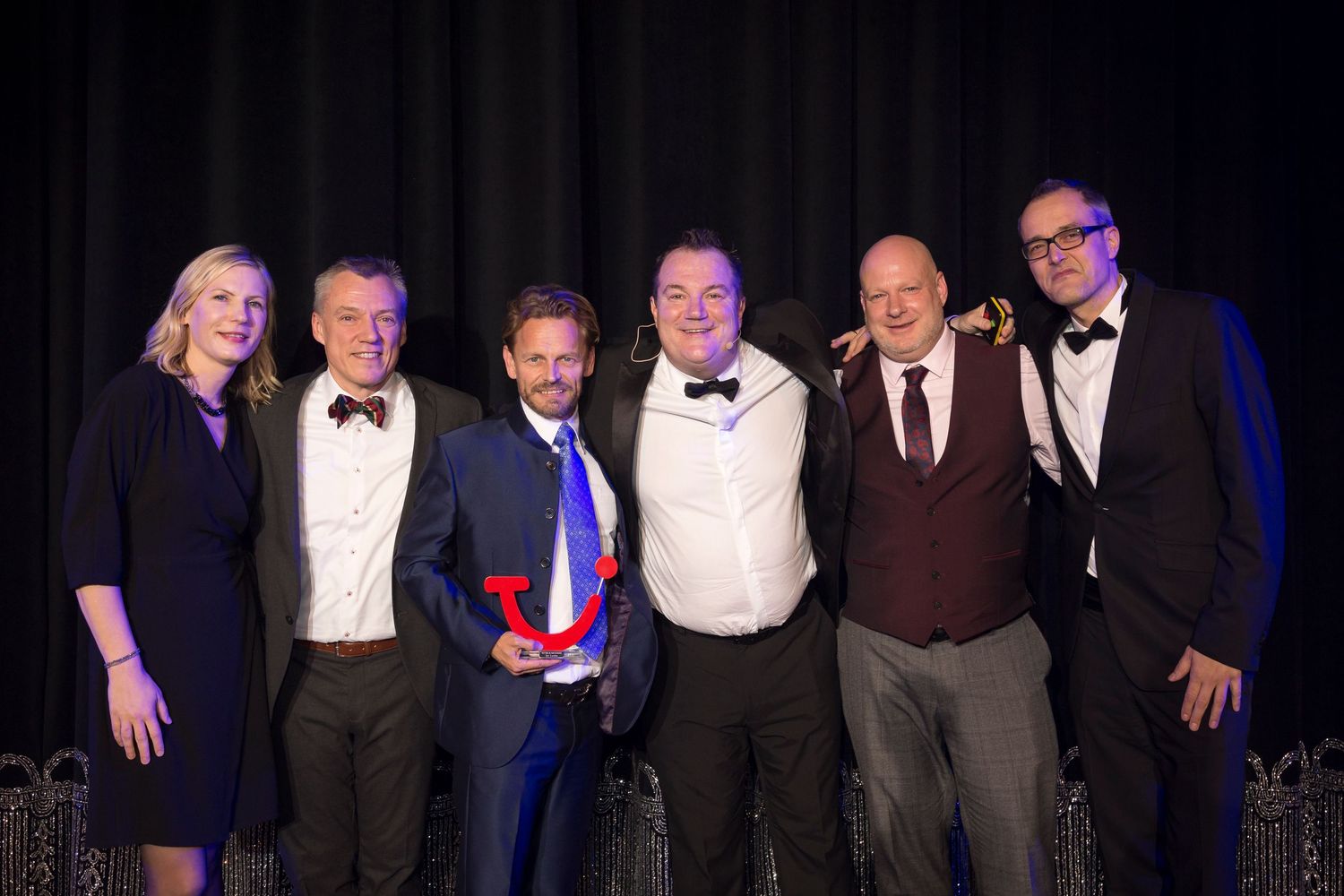 Group of six professionals posing together at an awards ceremony, one holding a trophy, dressed in formal attire.