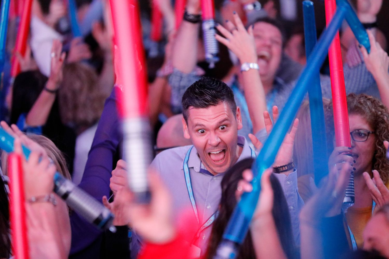 Excited crowd waving red and blue lightsabers at a Star Wars themed party event.