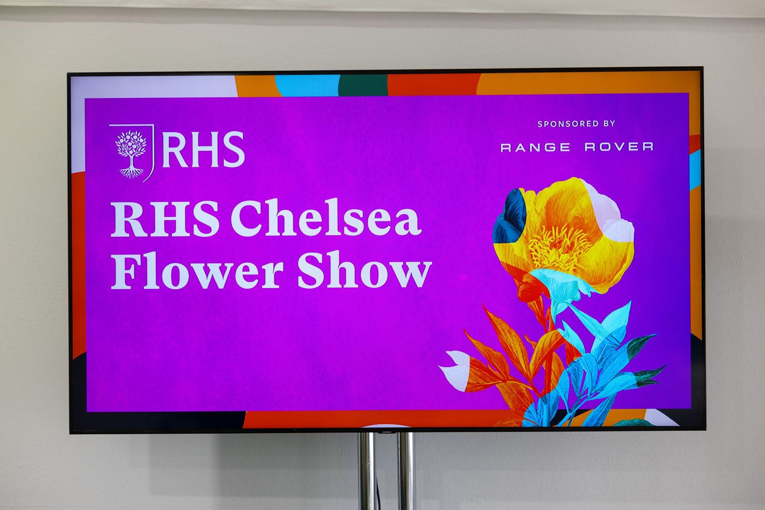 RHS Chelsea Flower Show promotional display screen sponsored by Range Rover with colorful floral graphics.