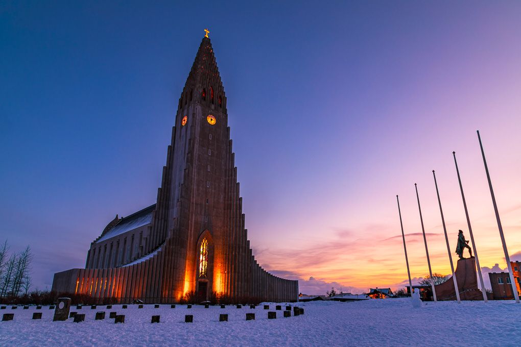 Hallgrimskirkja church in Reykjavik Iceland stands tall against a purple and orange sunset sky.