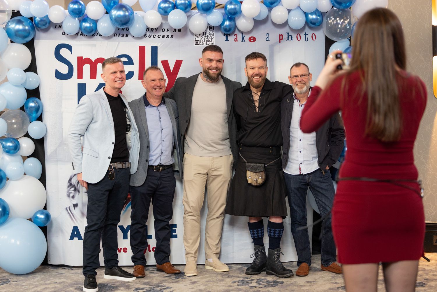 Guests posing for photographs at a book launch in Bedfordshire, captured with professional event photography against a branded backdrop