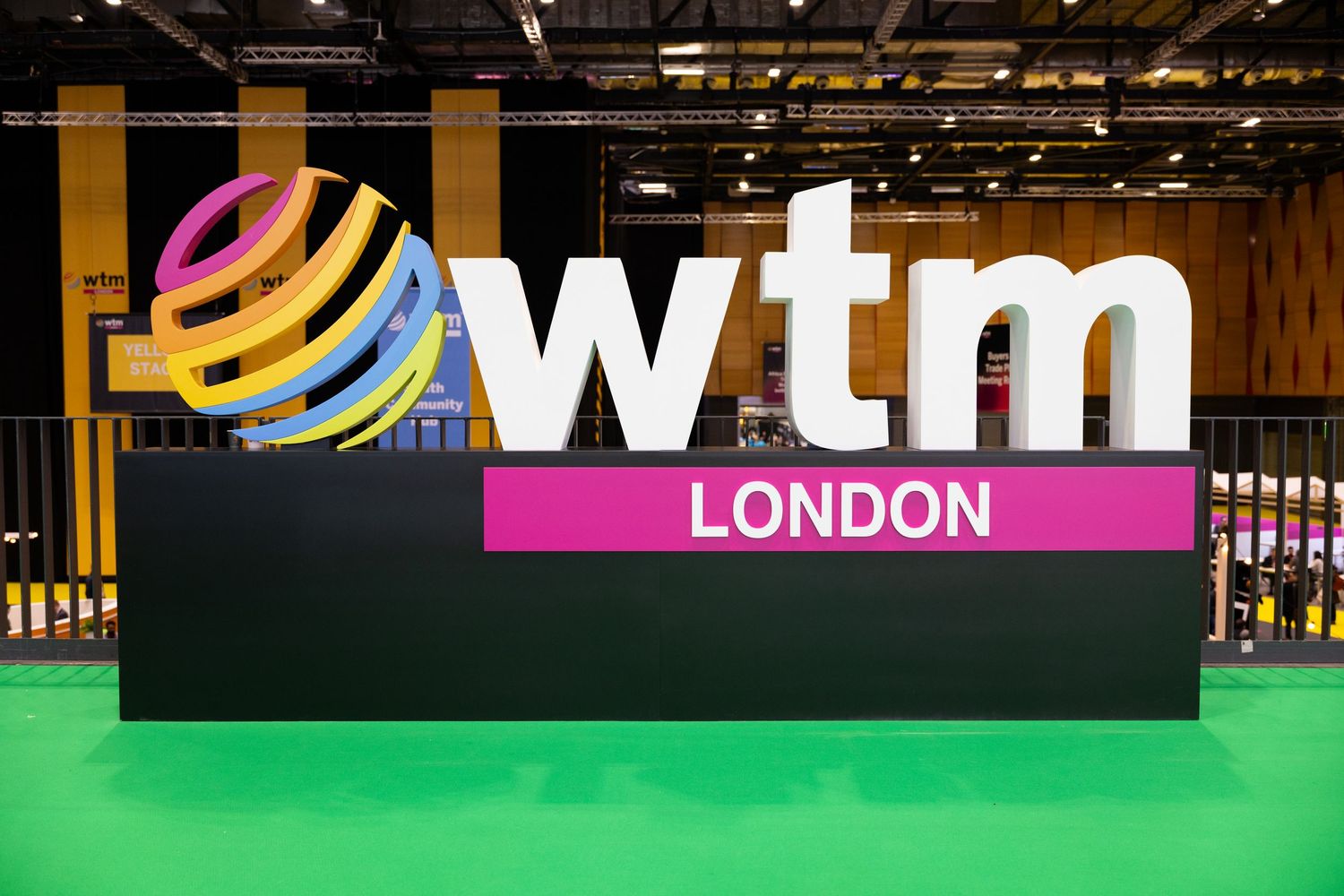 WTM London trade show sign with colorful globe logo on green floor at exhibition venue.