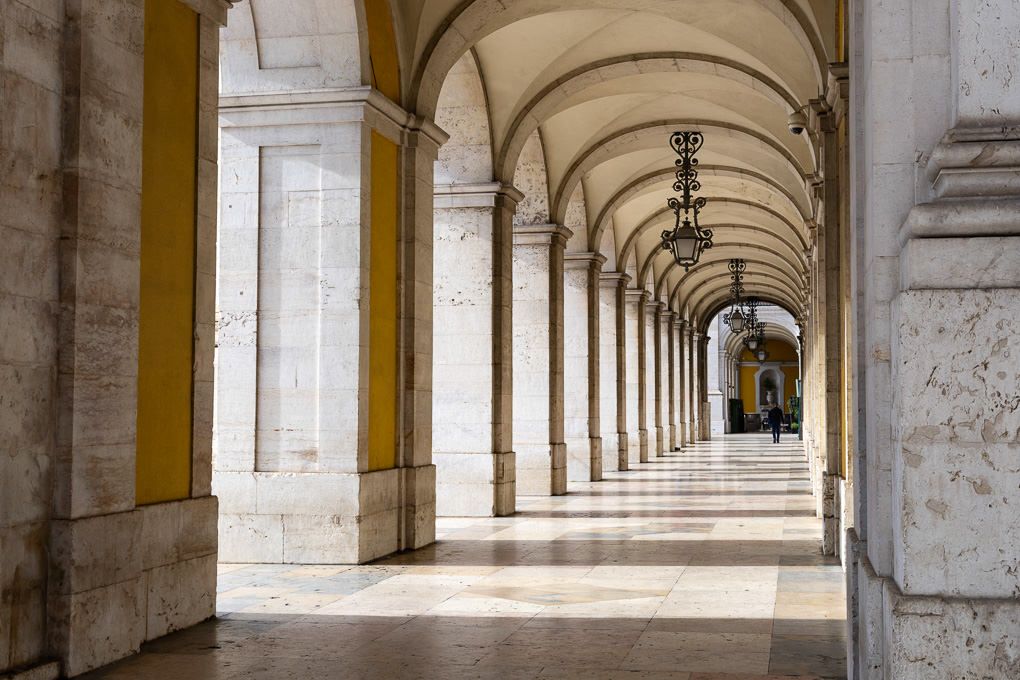 Classical arched colonnade with yellow pillars and vaulted ceiling creates a long symmetrical corridor in historic architecture.