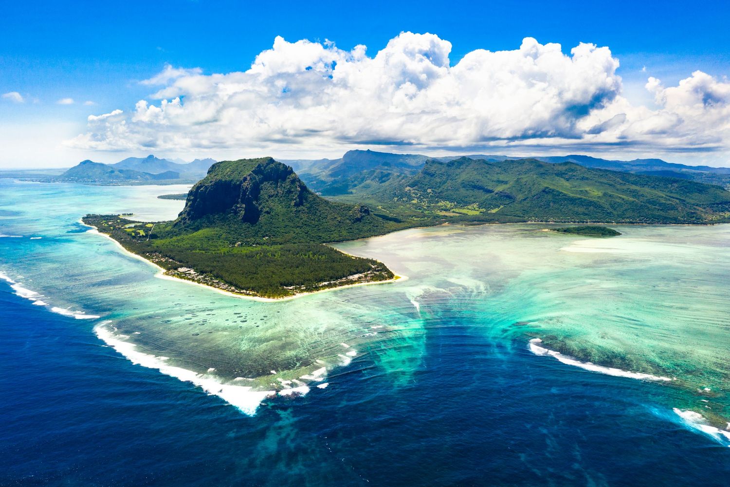 Aerial view of Le Morne Peninsula in Mauritius with turquoise lagoon and mountain backdrop, captured for tourism marketing.